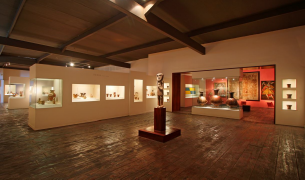 Sala de museo arqueológico en Lima exhibiendo vasijas de cerámica precolombina y estatuillas de culturas prehispánicas en vitrinas iluminadas.